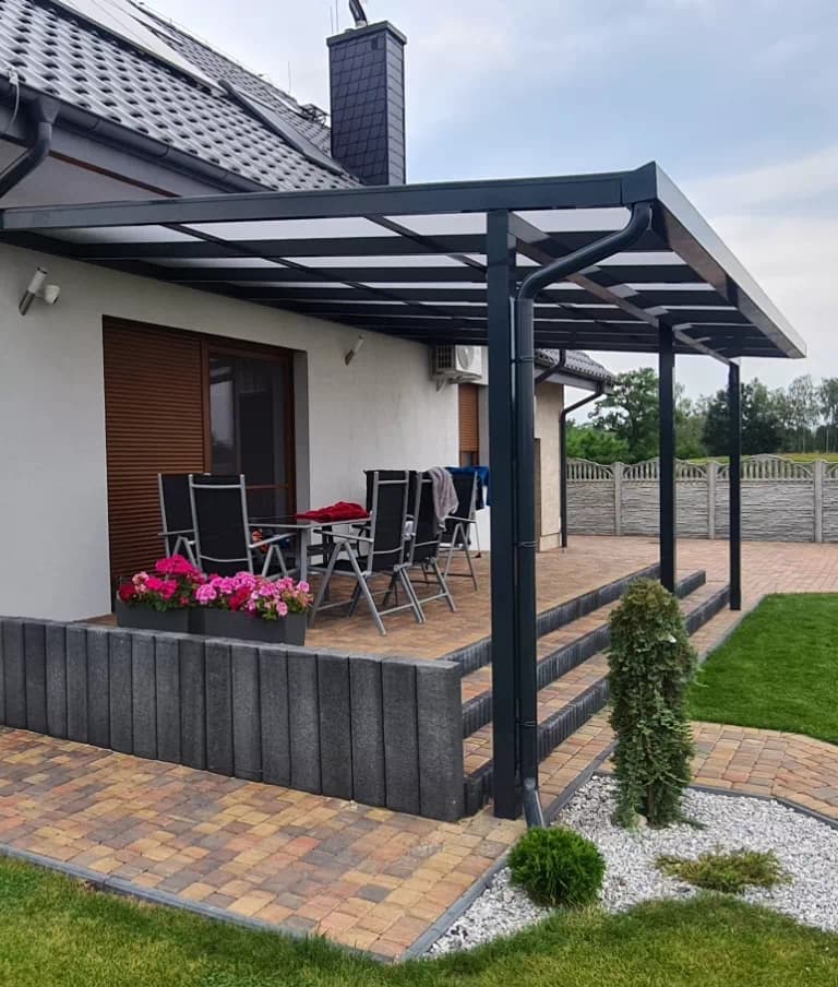 Daszki i zadaszenia. Zadaszenie tarasu na grafitowych słupach z rynną przy domu jednorodzinnym